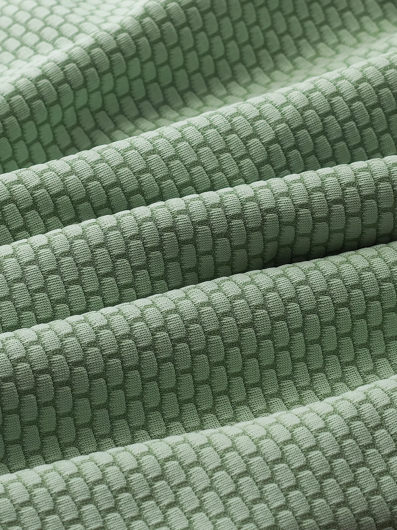 Close folded view of a green WellDoneTex mesh sample with repeating cellular surface pattern
